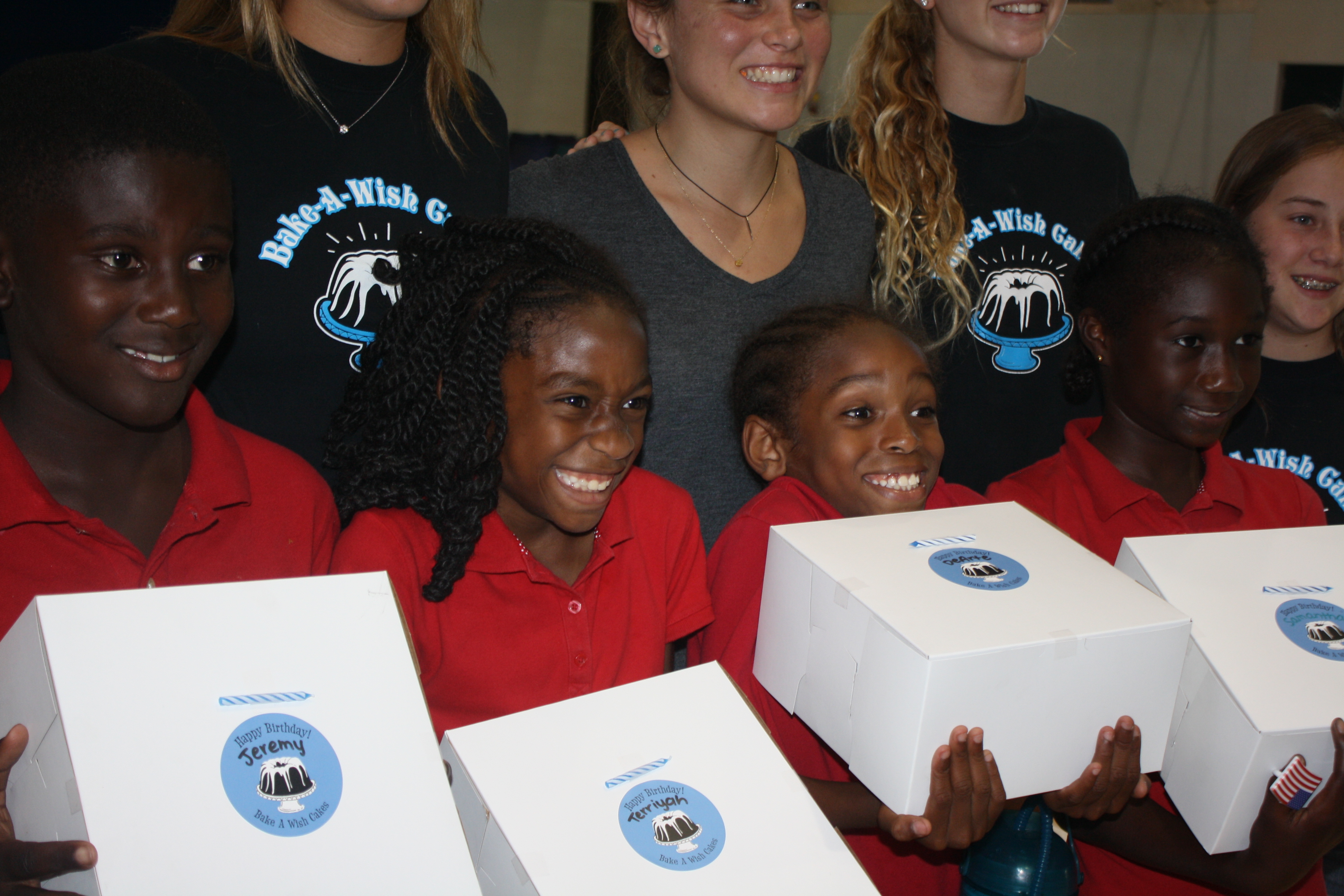 Children in school uniforms holding Bake-A-Wish cake boxes with volunteers