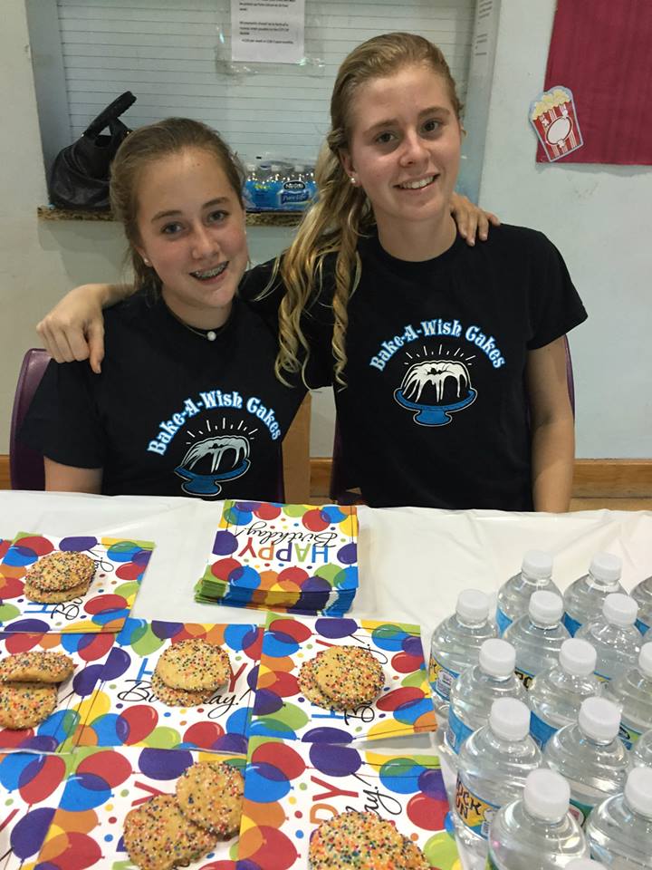 Two volunteers with decorated treats and water bottles at community event