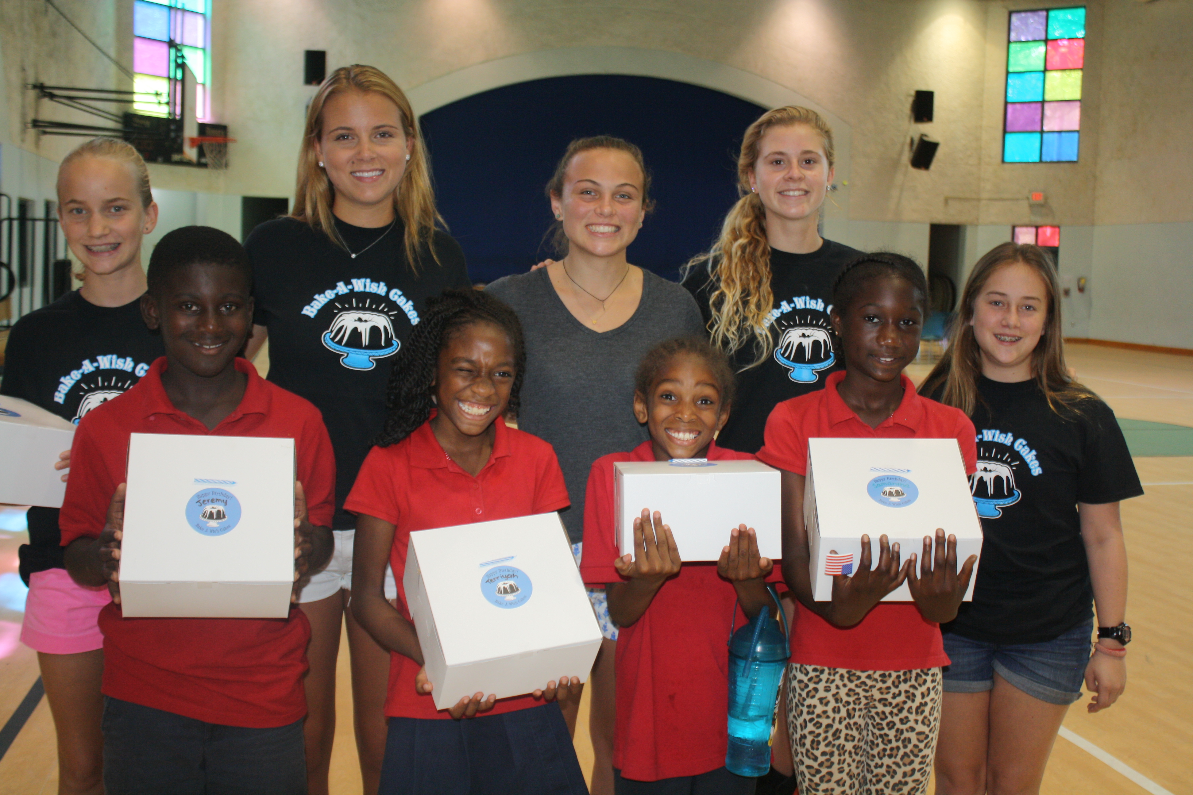 Group photo with volunteers and children holding cake boxes in gymnasium