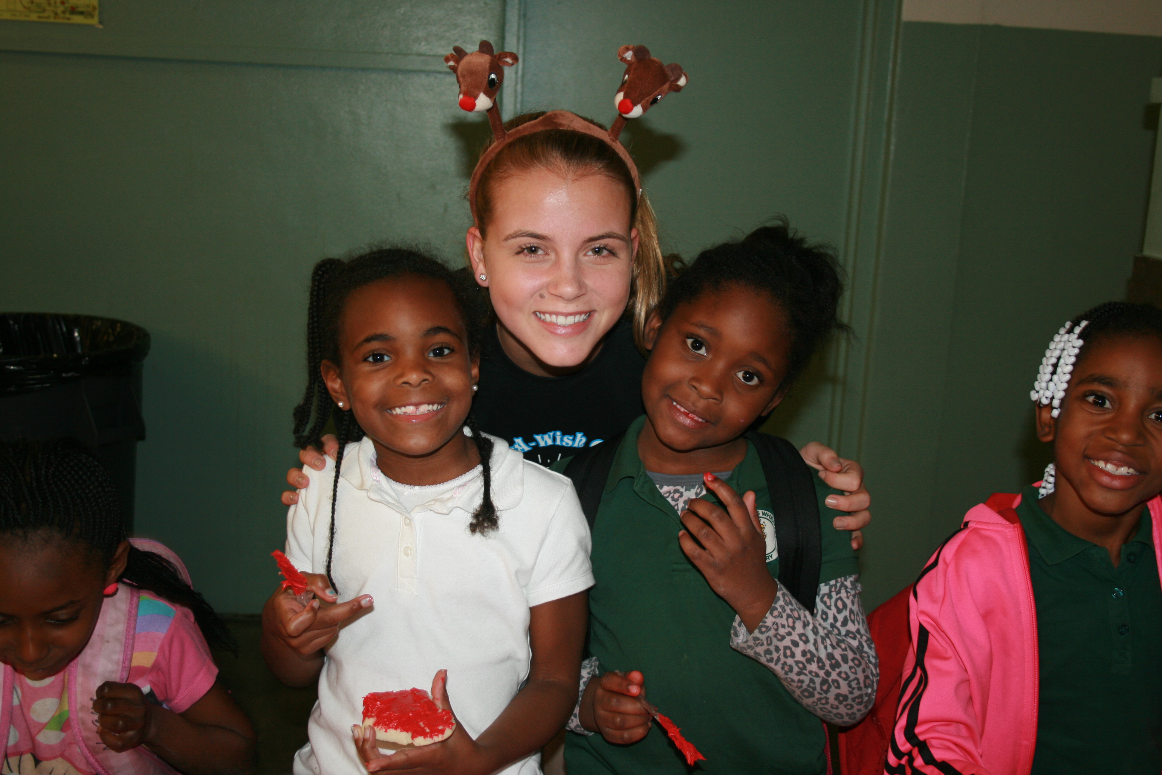 Volunteer wearing reindeer antlers with smiling children during holiday celebration