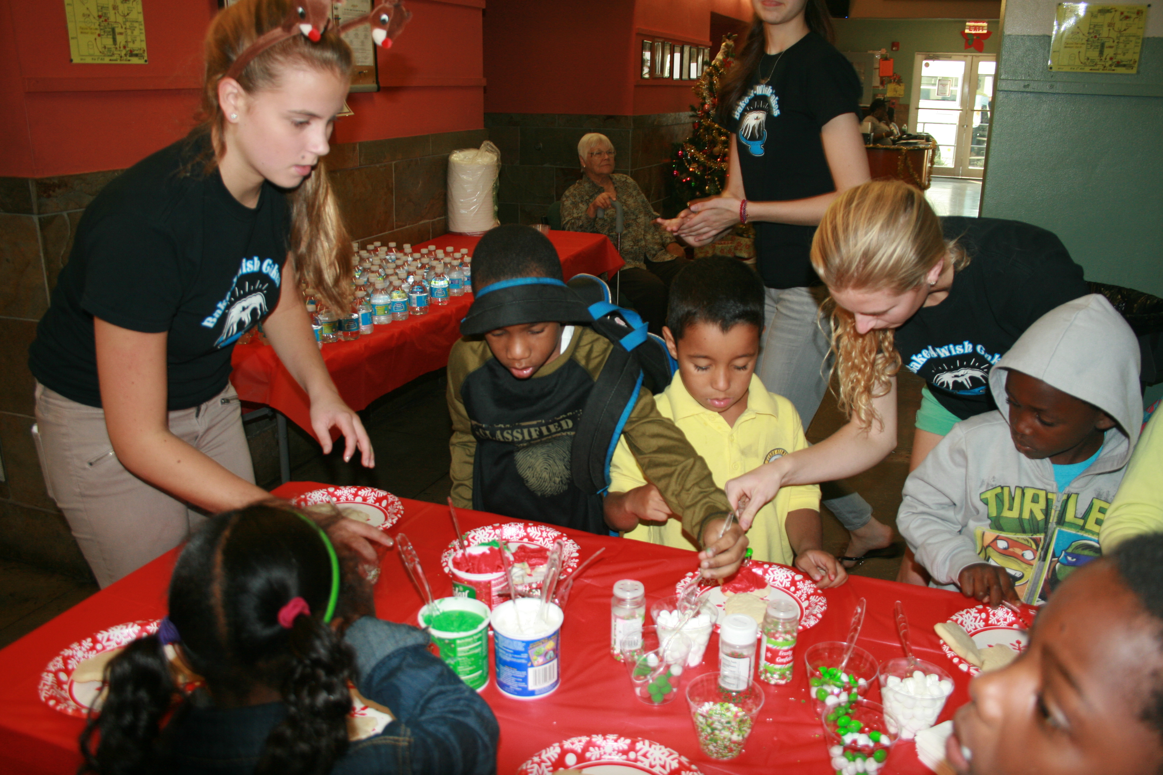 Bake-A-Wish volunteers helping children decorate cookies at festive holiday tables