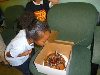 Young child looking down at opened cake box containing chocolate bundt cake