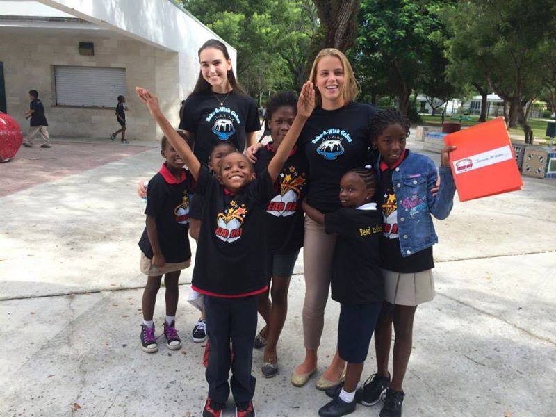 Volunteers with children from Read On! program outdoors, child waving enthusiastically