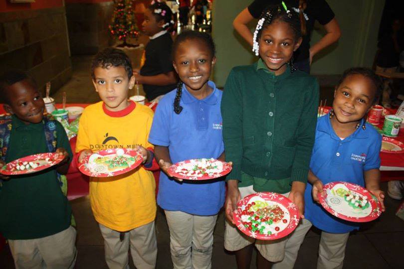 Five children in colorful school uniforms proudly holding their decorated cookie plates
