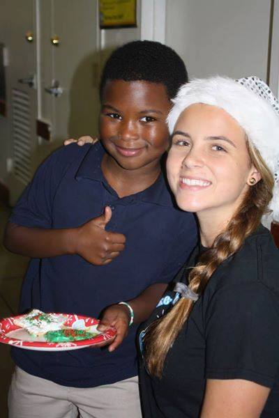 Volunteer in Santa hat with young boy holding decorated cookie plate, both smiling