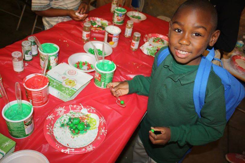 Smiling young boy in green uniform at cookie decorating table with festive supplies