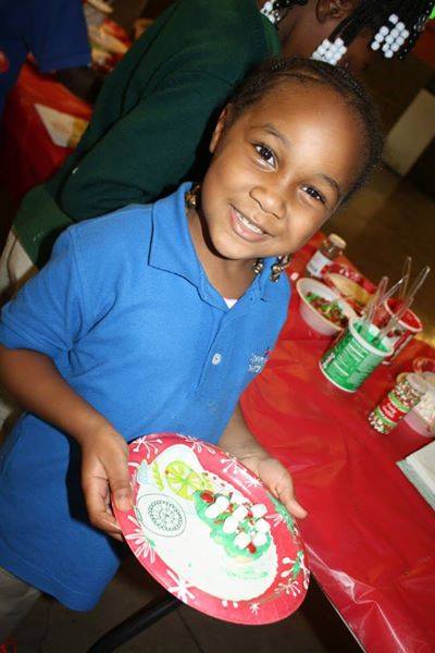 Smiling girl in blue uniform proudly holding decorated holiday cookie