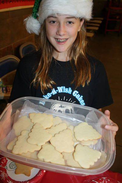 Bake-A-Wish volunteer in Santa hat holding container of fresh sugar cookies