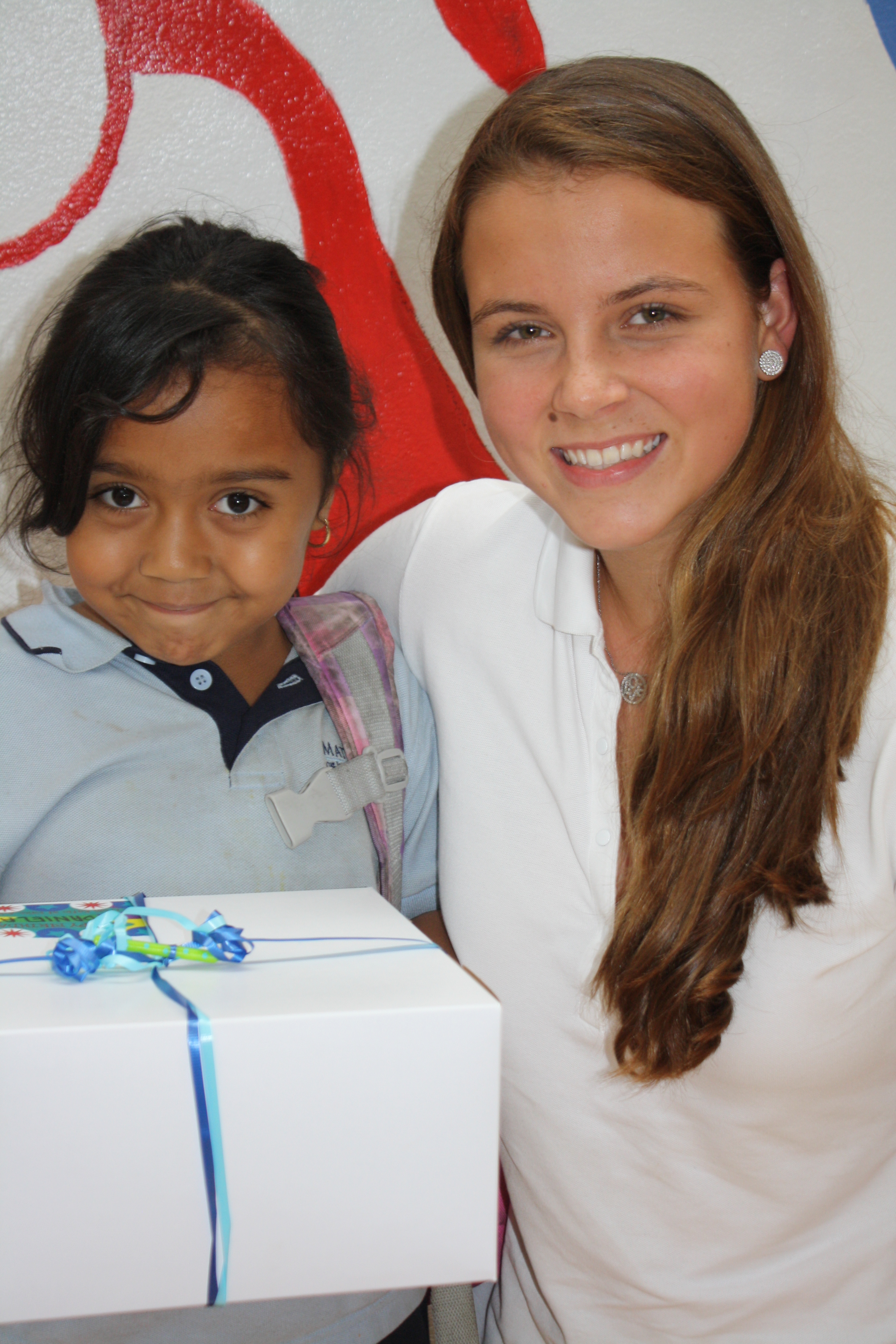 Volunteer with young girl holding birthday cake box with blue ribbon
