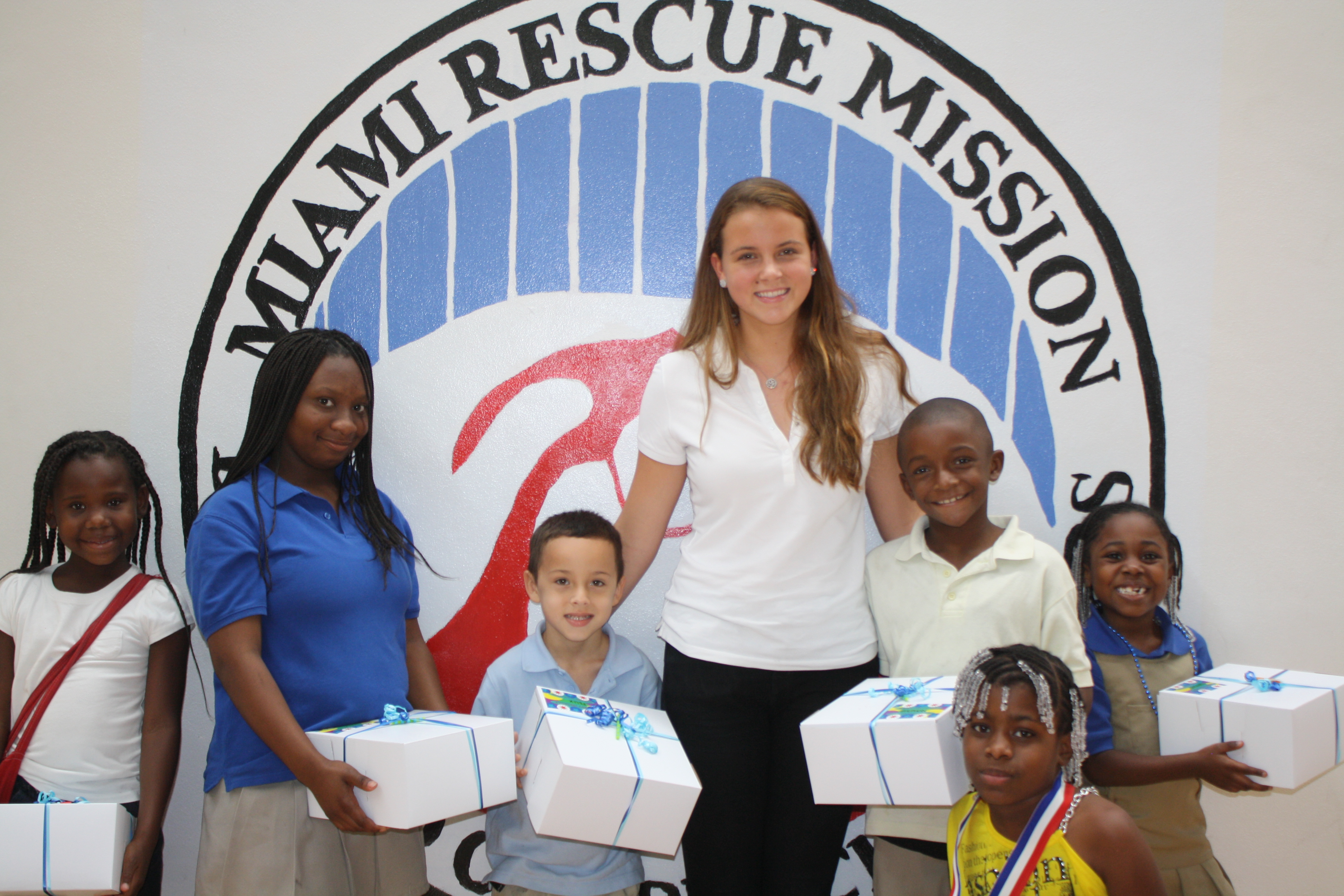 Group photo at Miami Rescue Mission with volunteers and children holding multiple cake boxes