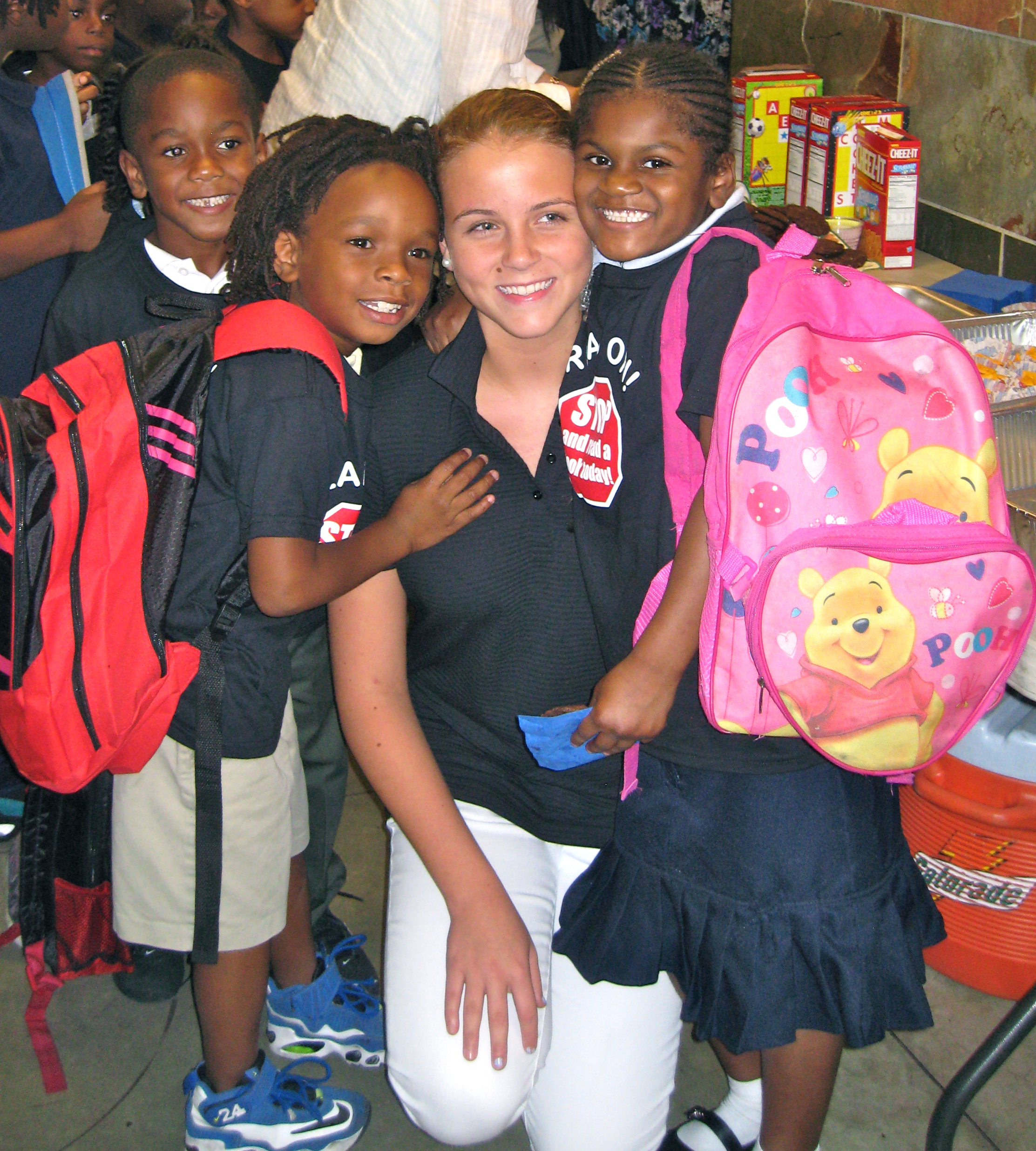 Volunteer surrounded by children with backpacks showing strong community bonds