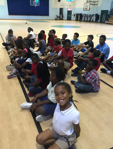 Children sitting in school gymnasium, smiling child in foreground