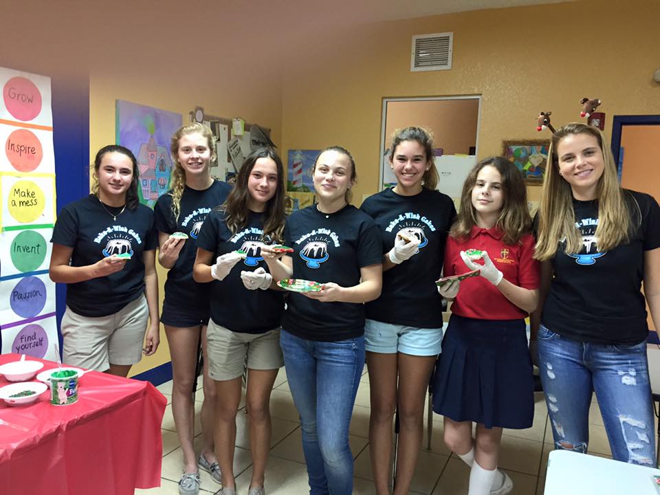 Bake-A-Wish volunteers with student holding decorated cookies in classroom